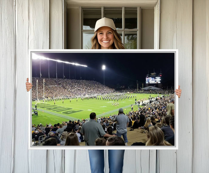 A painting depicting the Purdue Boilermakers football game at Ross-Ade Stadium is illuminated under gallery-quality lights.