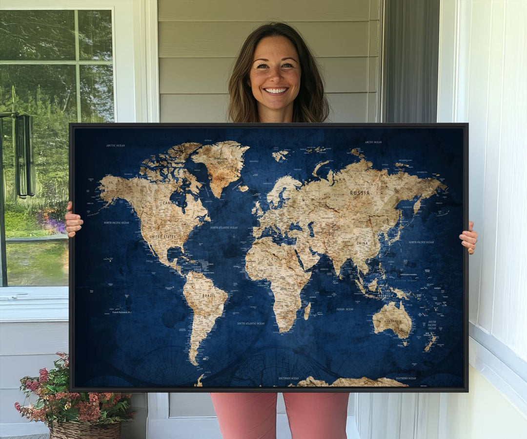 A large framed world map canvas print features beige landmasses set against a grunge-stained deep blue ocean background, creating an intriguing piece of wall art.