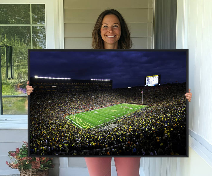 A painting of the packed Michigan Wolverines football stadium at night.