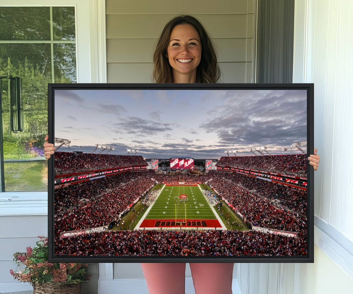 The wall art captures a stunning scene of Raymond James Stadium bathed in the warm hues of sunset. The sky, filled with clouds, provides a dramatic contrast to the vibrant lighting on the field, encapsulating the dynamic energy of a football game.