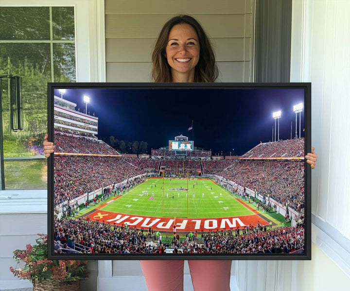 A NC State Wolfpack Football Team print of Carter-Finley Stadium at night features WOLFPACK illuminated brightly in the end zone grass.