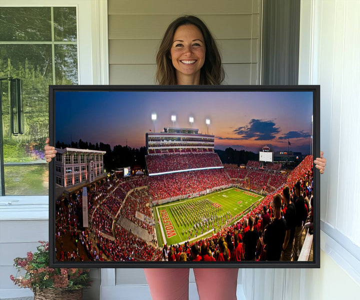 A print of a bustling Carter-Finley Stadium at dusk, featuring fans and a band, captures the essence of NC State Wolfpack football.