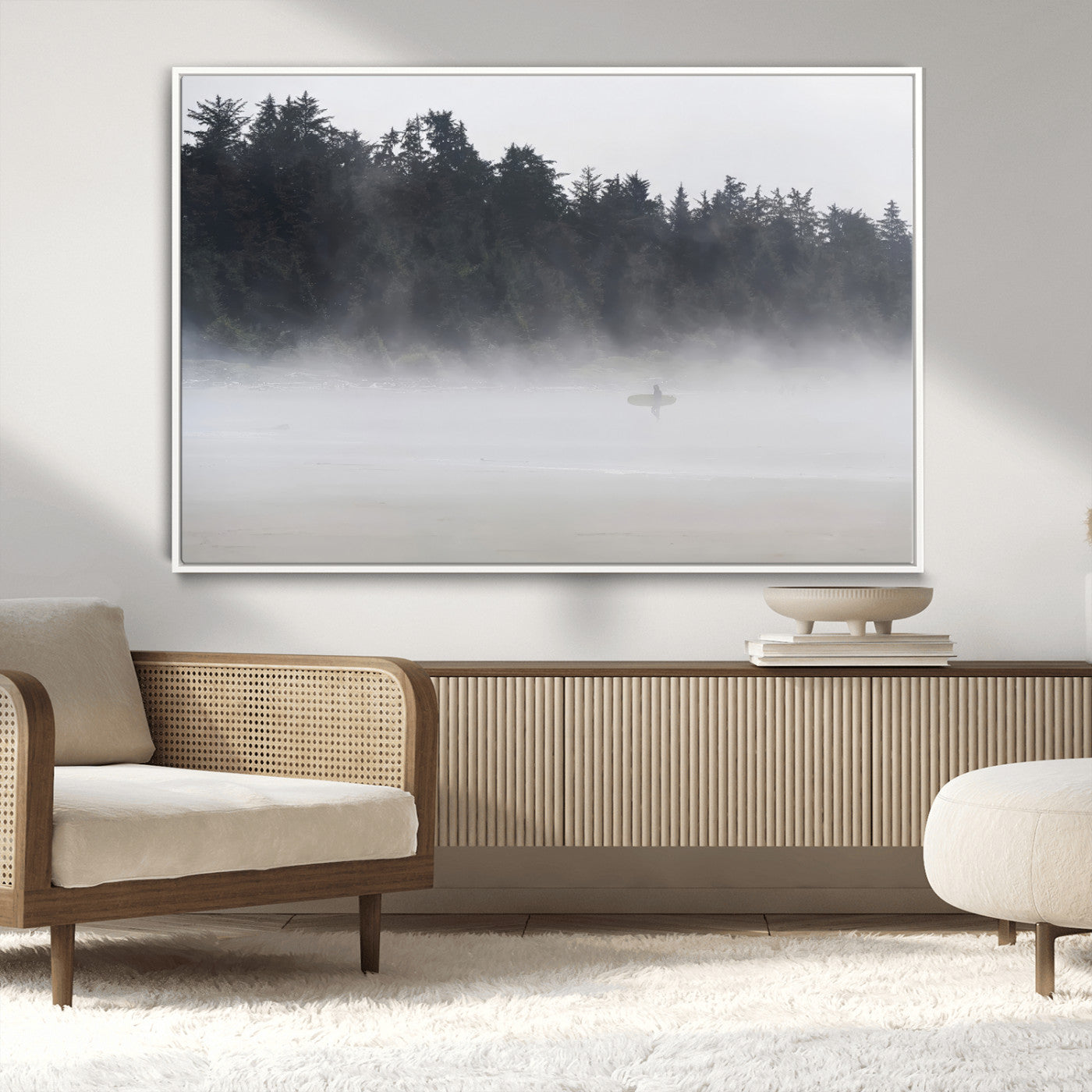 A lone surfer carrying a board through a misty shoreline, surrounded by dense trees and fog, creating a peaceful and mysterious coastal scene.