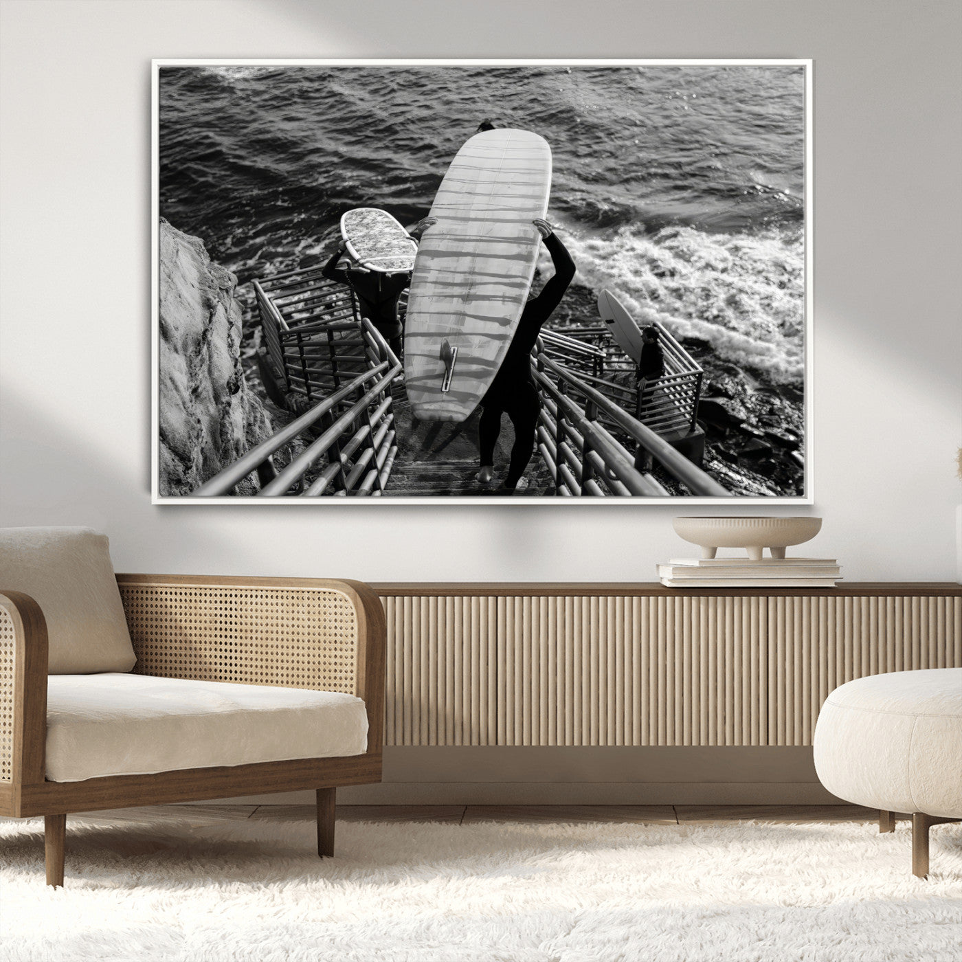 Black and white photo of surfers carrying boards down a rugged cliffside stairway, capturing a bold and adventurous coastal scene.