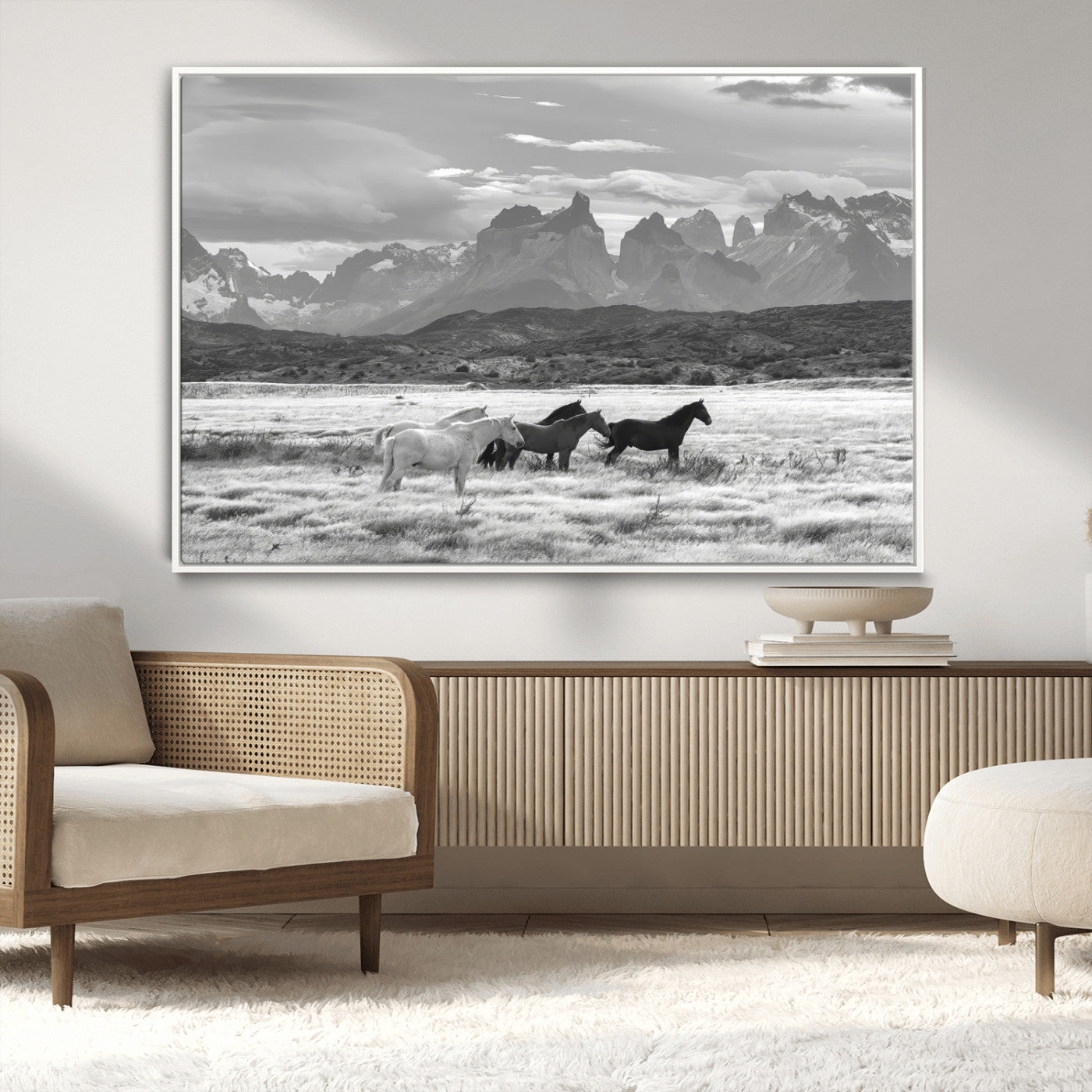 A black and white landscape of wild horses grazing in a vast grassland with towering mountains in the background, creating a moody and rustic western aesthetic.