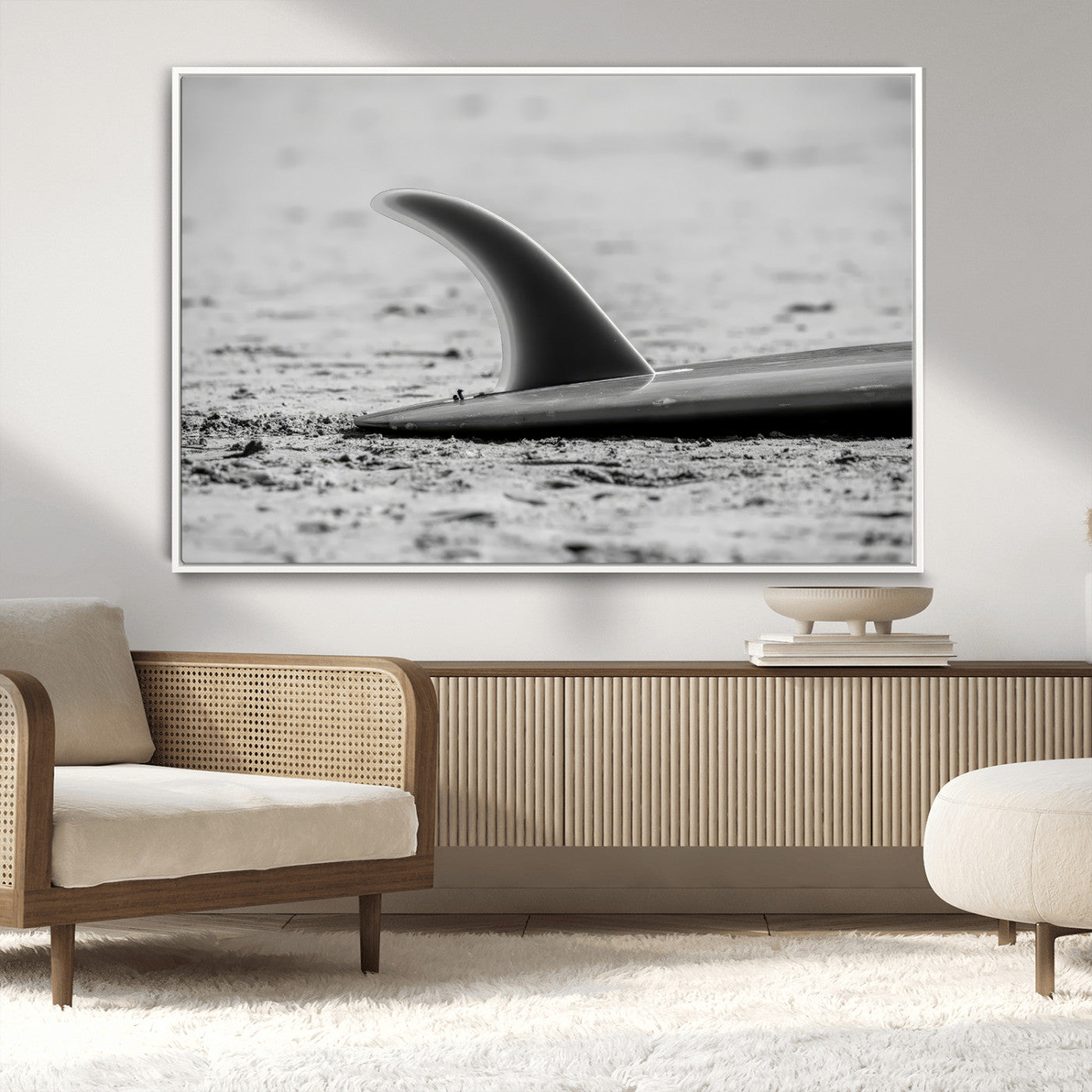 A black and white close-up of a surfboard fin resting on the sandy shore, highlighting minimalist beach aesthetics and classic surf culture.
