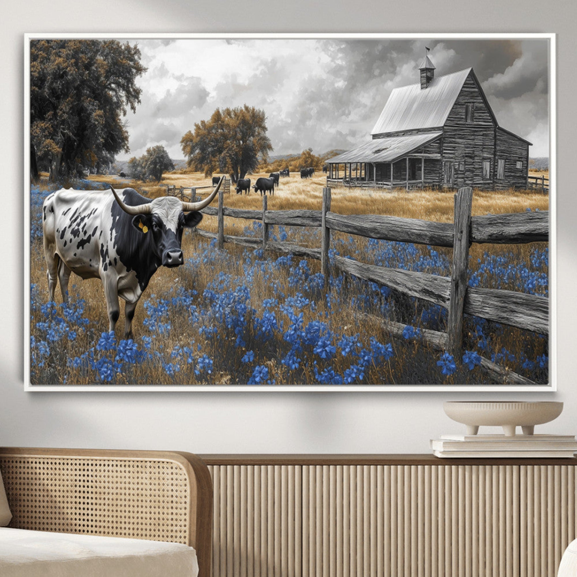 A Texas longhorn stands in front of a rustic barn and wooden fence, with bluebonnets and grazing cattle under dramatic skies.