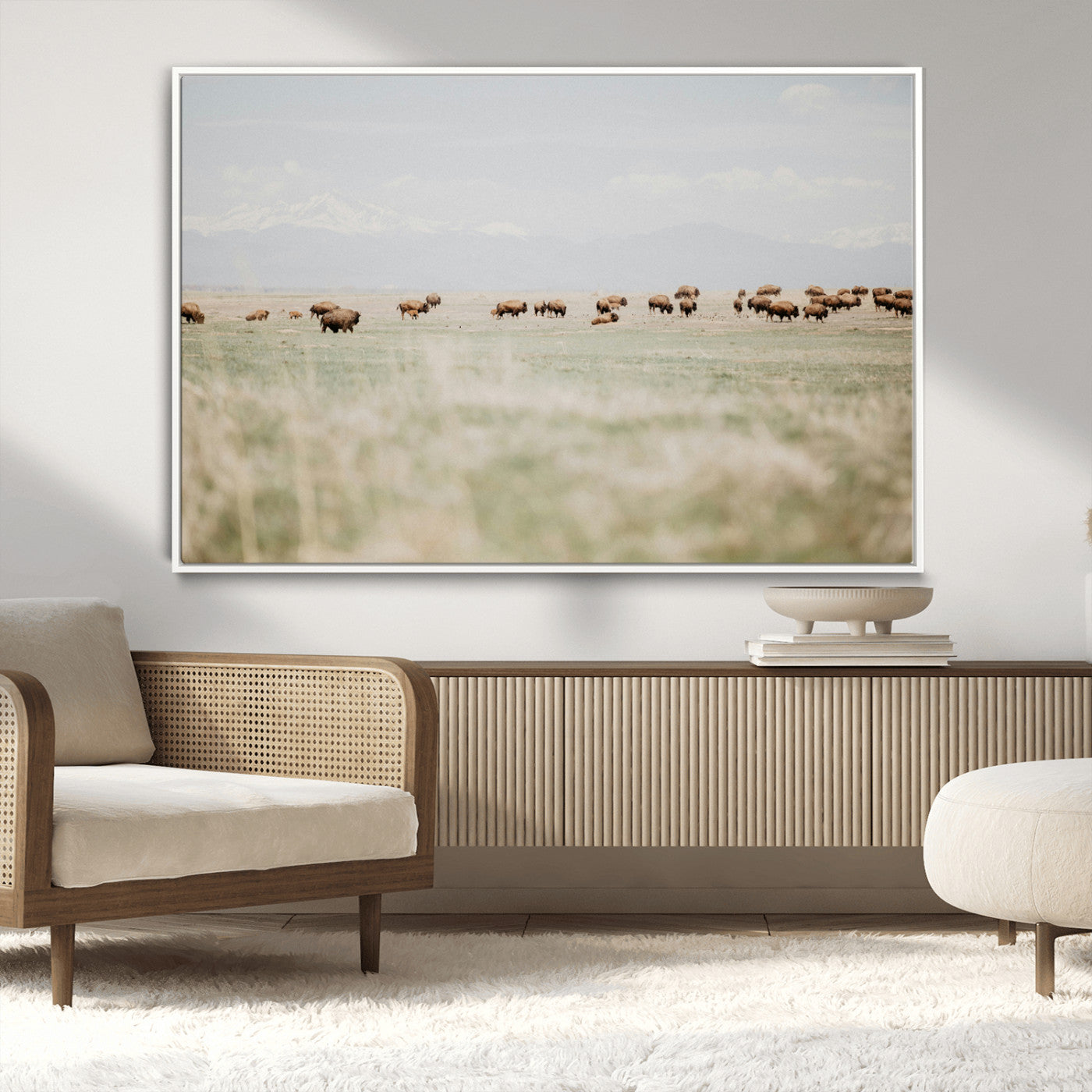 A herd of bison grazing in an open prairie with distant mountains under a soft sky, creating a serene and rustic Western landscape.