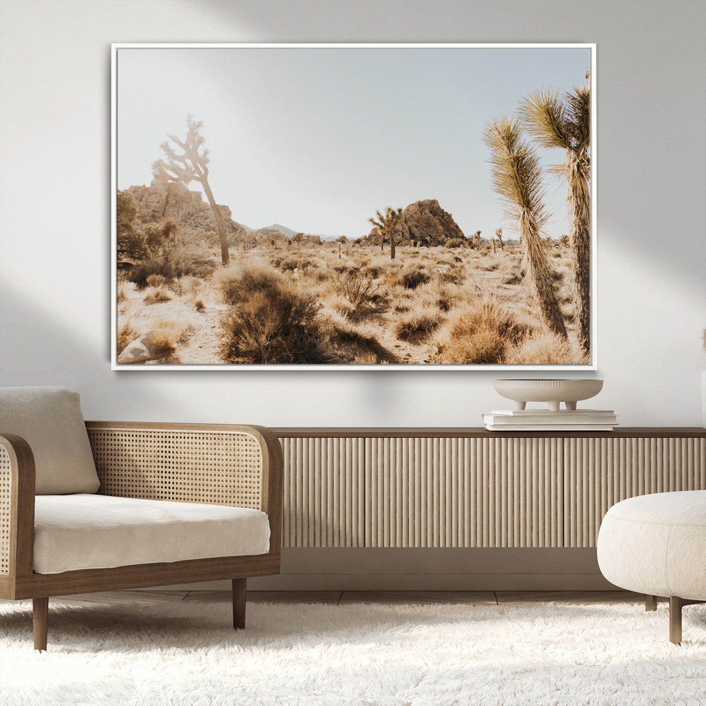 Sunlit desert landscape featuring Joshua trees, rocky formations, and dry bushes under a clear sky.