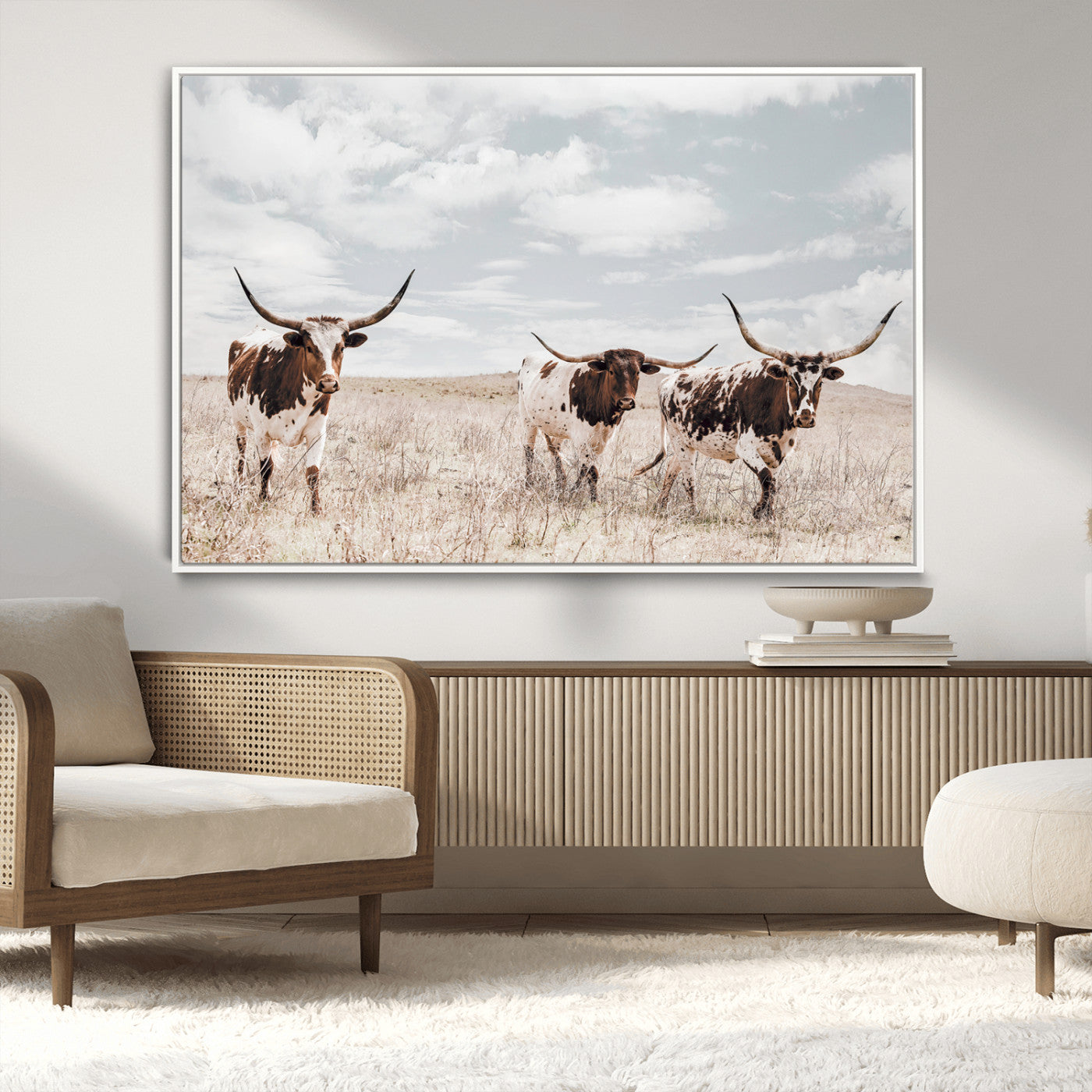 Three Texas Longhorn cattle walking through a dry grassy field under a partly cloudy sky.