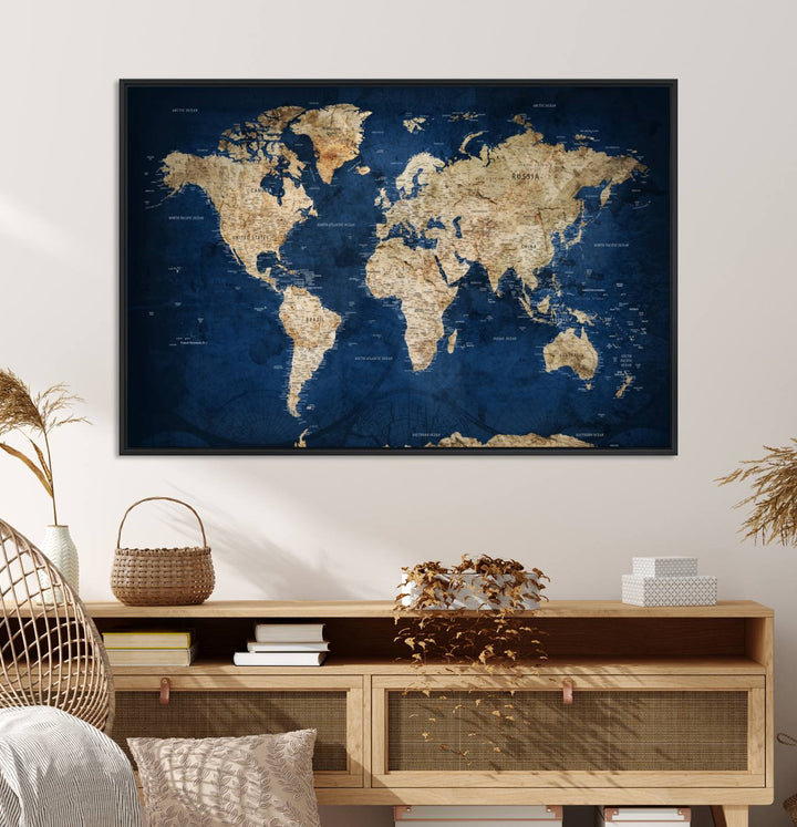 A large framed world map canvas print features beige landmasses set against a grunge-stained deep blue ocean background, creating an intriguing piece of wall art.