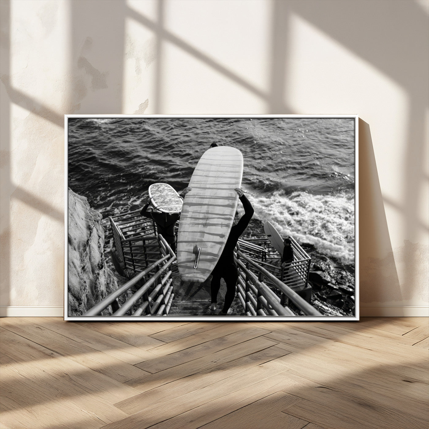 Black and white photo of surfers carrying boards down a rugged cliffside stairway, capturing a bold and adventurous coastal scene.
