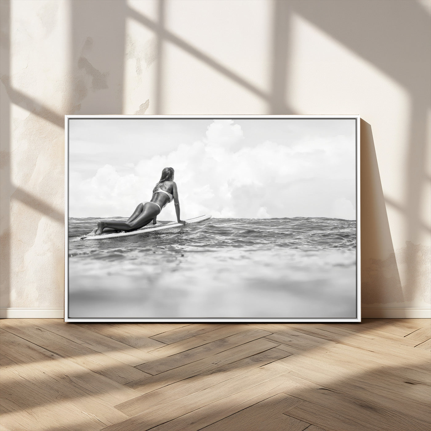 A black and white ocean scene featuring a surfer girl waiting on her board, gazing at the horizon, capturing a tranquil and adventurous coastal moment.