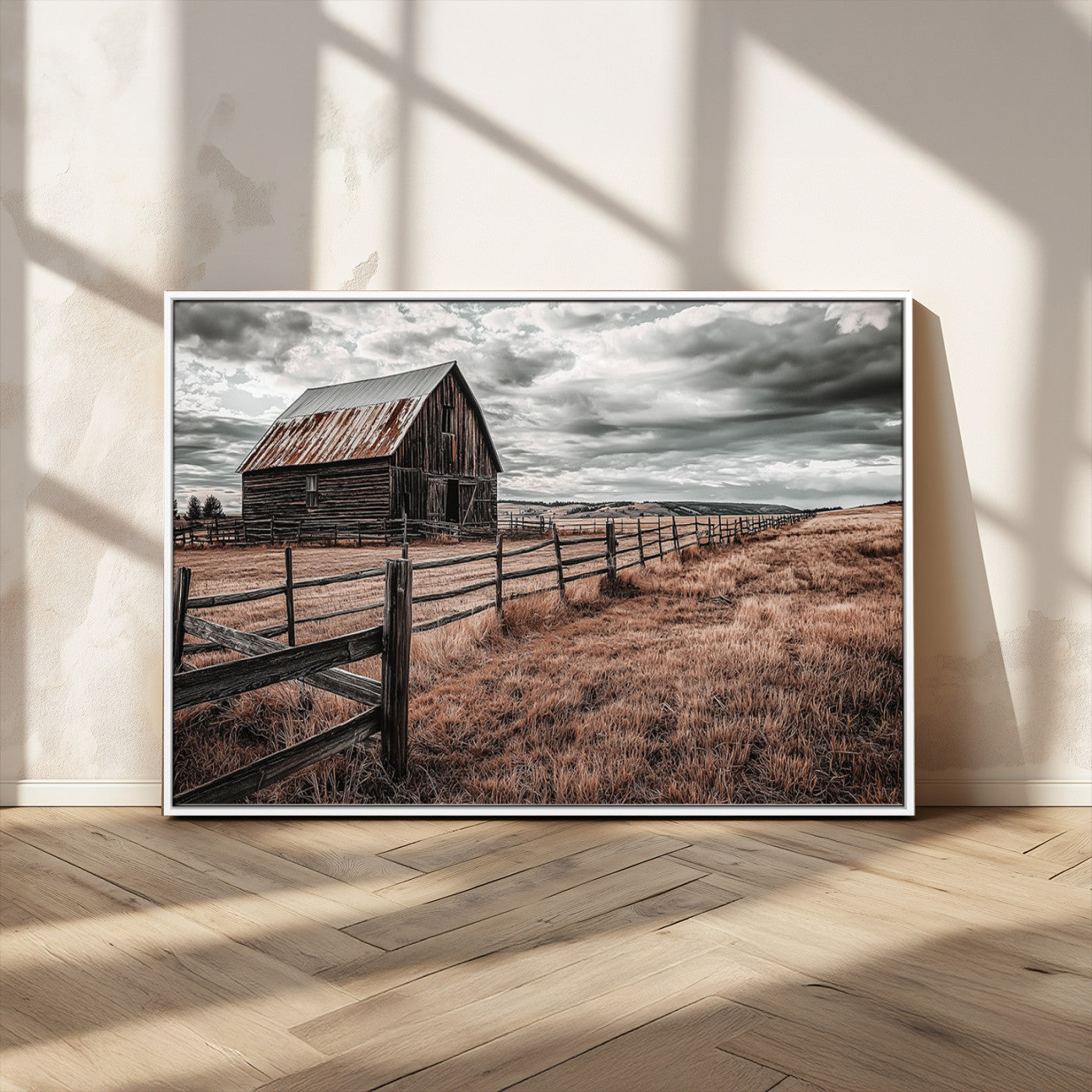 "Black-and-white photograph of a rustic barn with a weathered roof, surrounded by a wooden fence and vast golden fields under a moody sky."