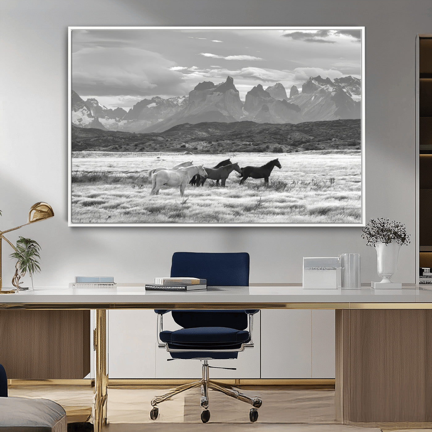 A black and white landscape of wild horses grazing in a vast grassland with towering mountains in the background, creating a moody and rustic western aesthetic.