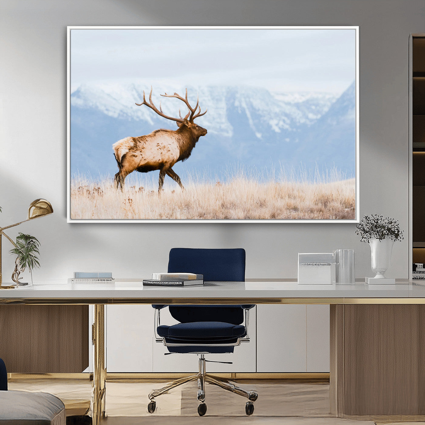 An elk walking on snowy grassland with majestic mountains in the background, ideal for rustic lodge or cabin wall decor.