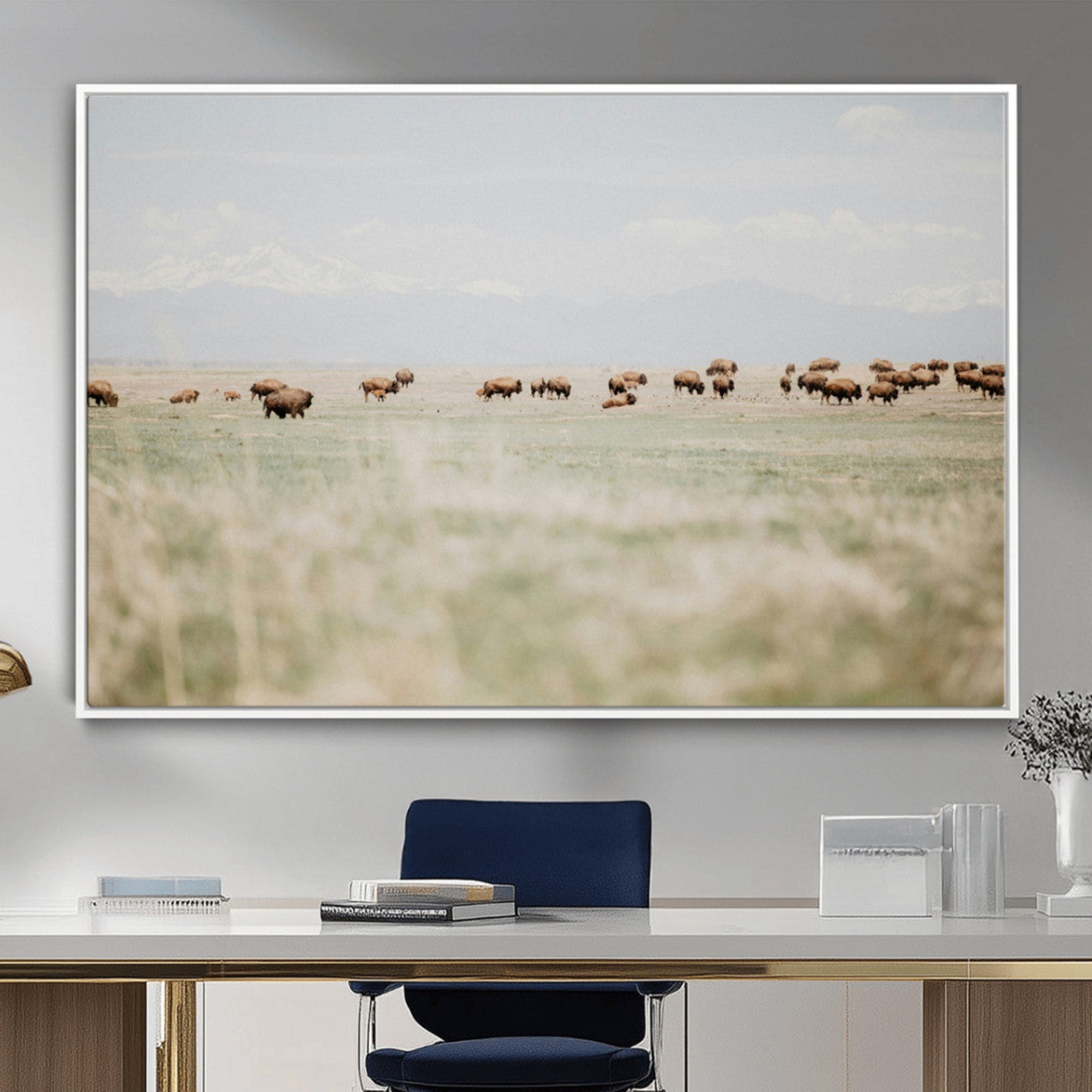 A herd of bison grazing in an open prairie with distant mountains under a soft sky, creating a serene and rustic Western landscape.