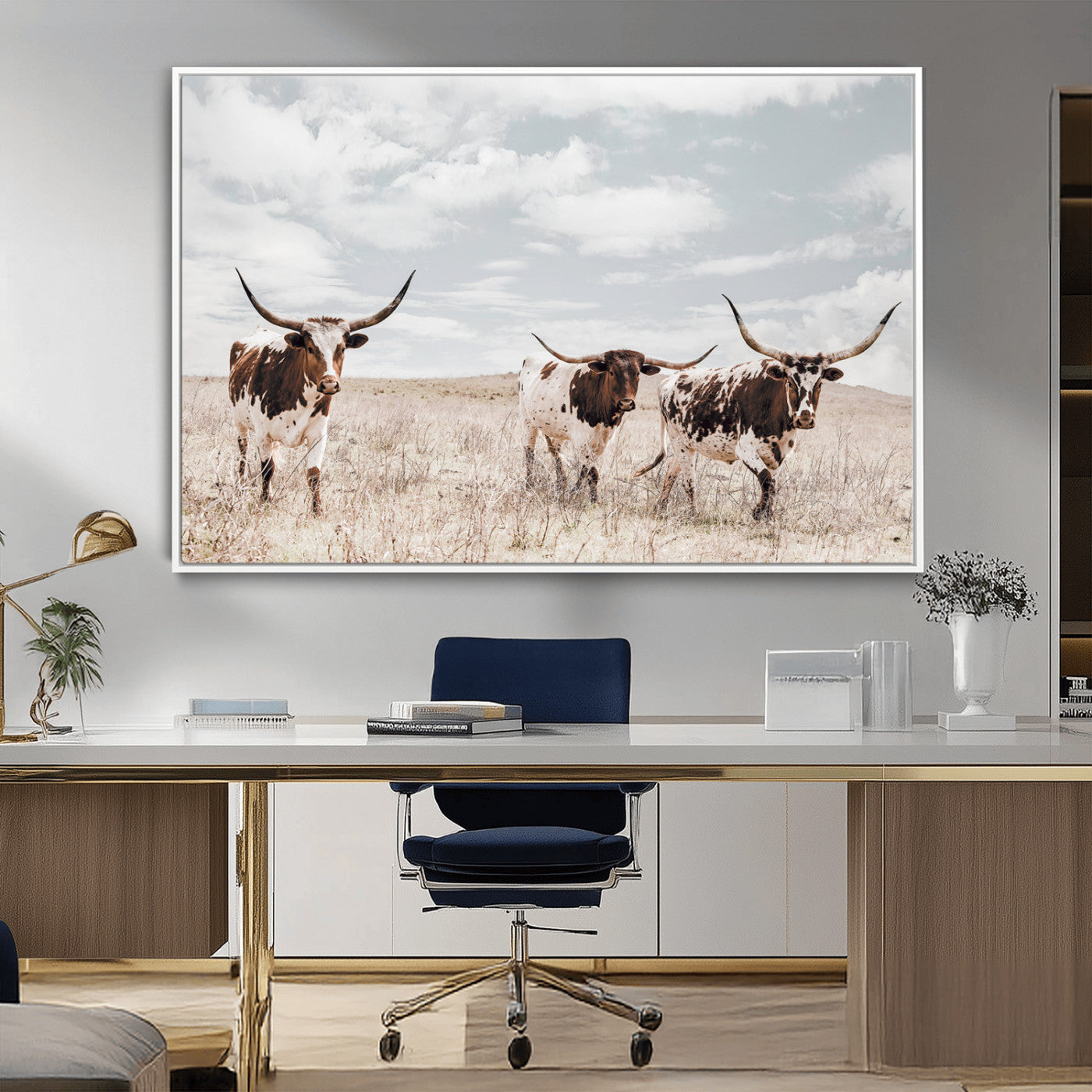Three Texas Longhorn cattle walking through a dry grassy field under a partly cloudy sky.