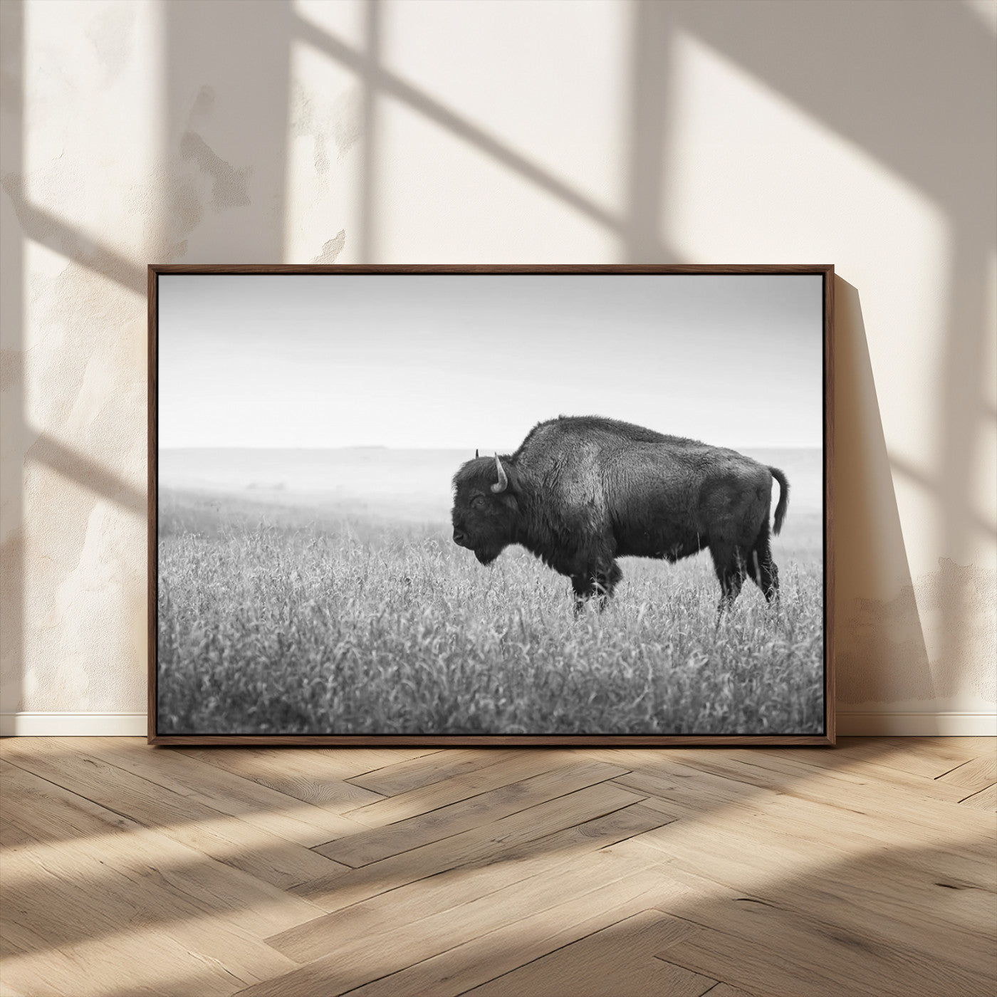 "Black and white image of a bison grazing in a vast field under an overcast sky."