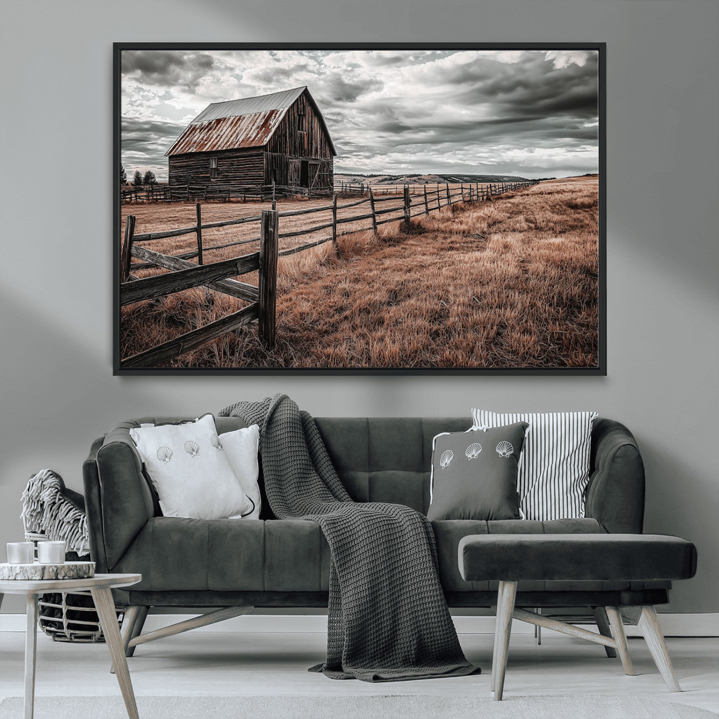 "Black-and-white photograph of a rustic barn with a weathered roof, surrounded by a wooden fence and vast golden fields under a moody sky."