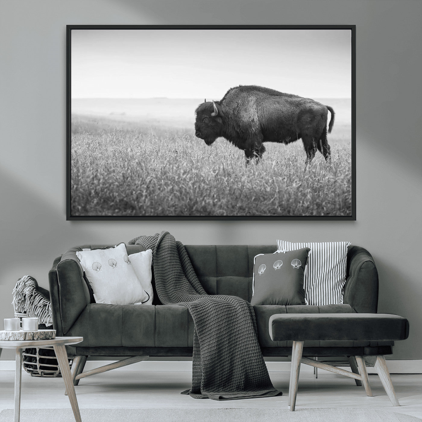 "Black and white image of a bison grazing in a vast field under an overcast sky."