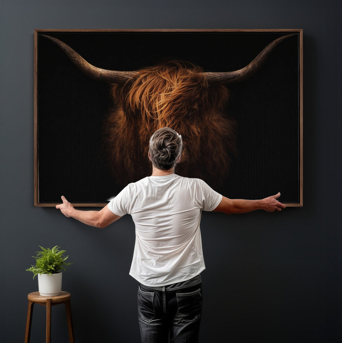 Man standing in front of a large framed picture of a Highland cow on a dark wall.