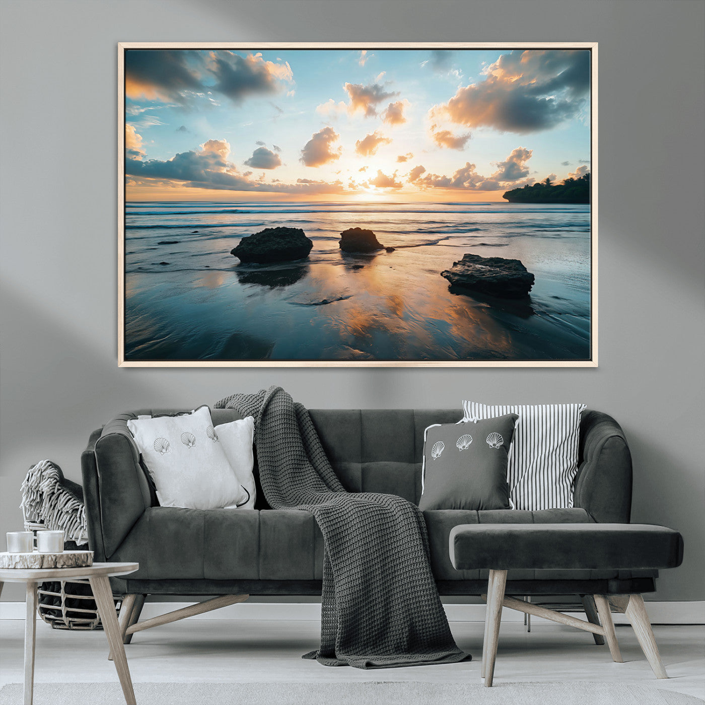 A serene beach at sunset with vibrant clouds, calm water, and rocks in the foreground reflecting the warm colors of the setting sun.