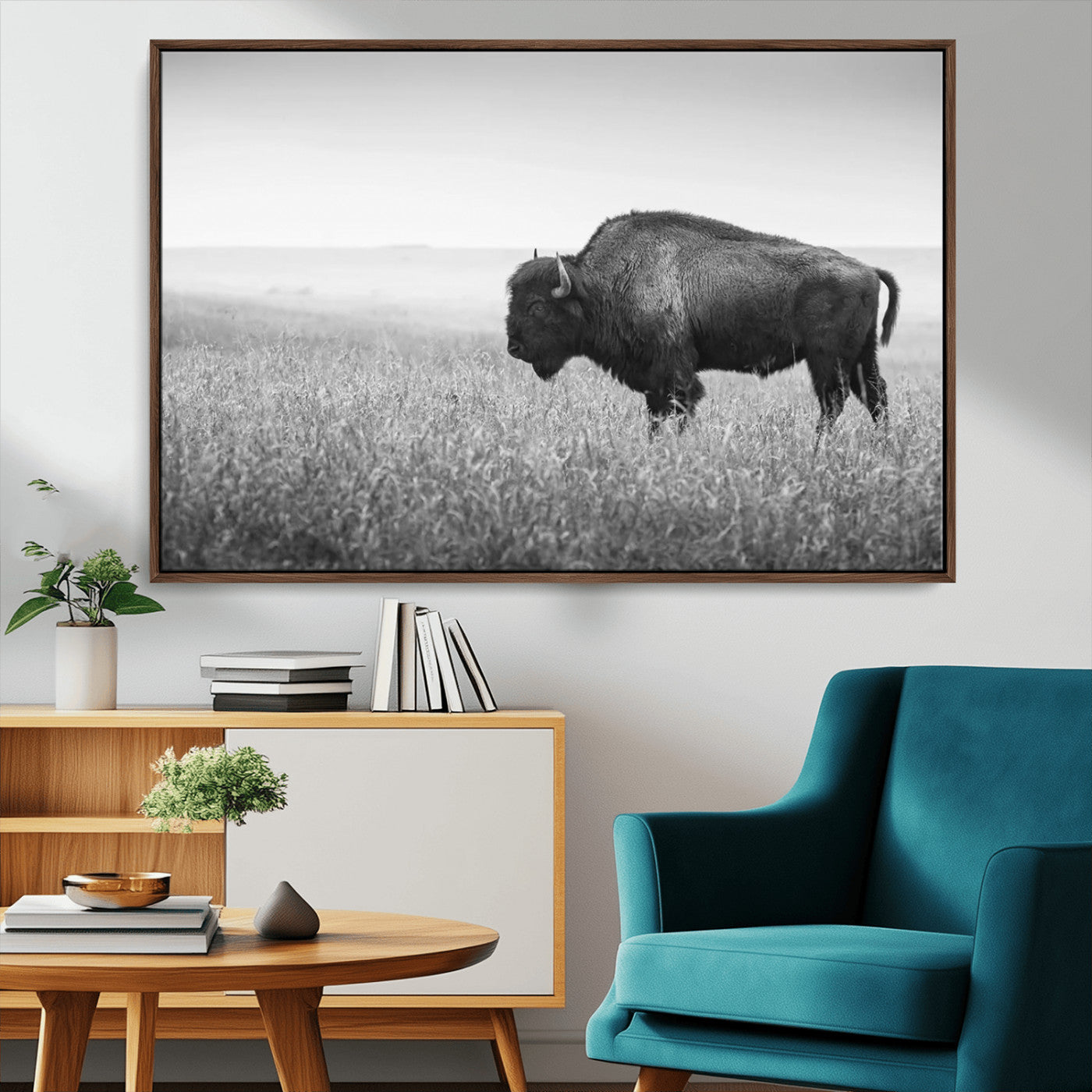 "Black and white image of a bison grazing in a vast field under an overcast sky."