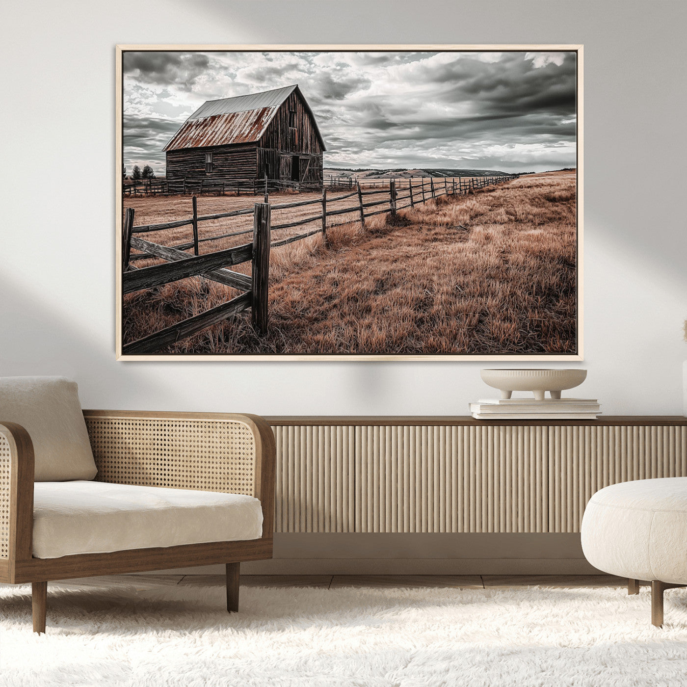 "Black-and-white photograph of a rustic barn with a weathered roof, surrounded by a wooden fence and vast golden fields under a moody sky."