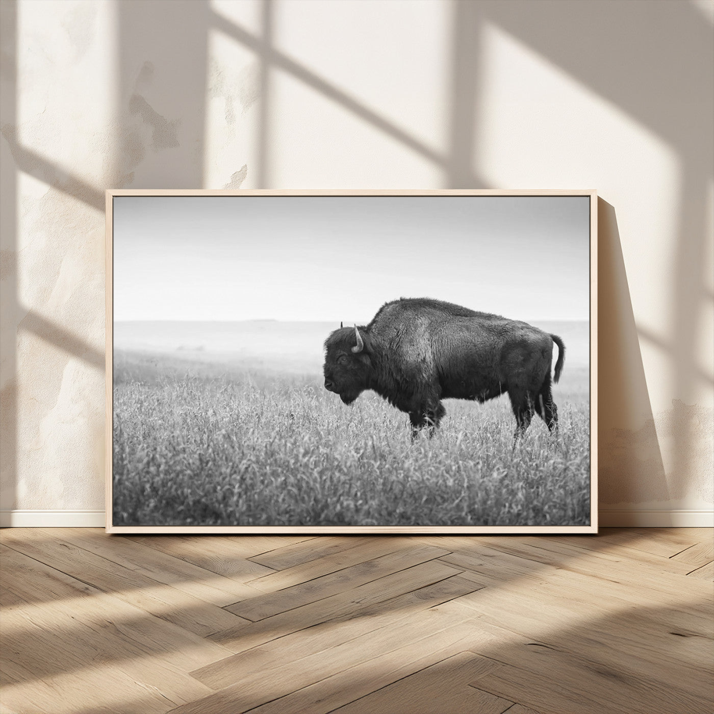 "Black and white image of a bison grazing in a vast field under an overcast sky."