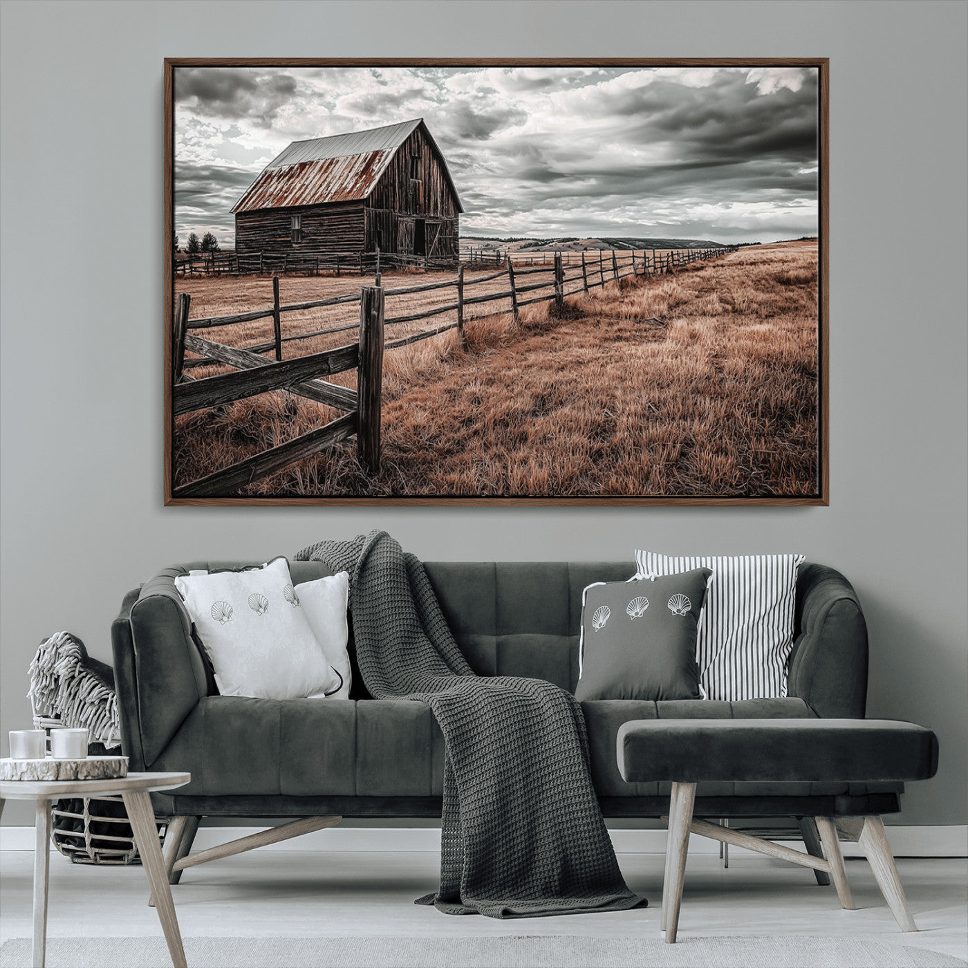 "Black-and-white photograph of a rustic barn with a weathered roof, surrounded by a wooden fence and vast golden fields under a moody sky."