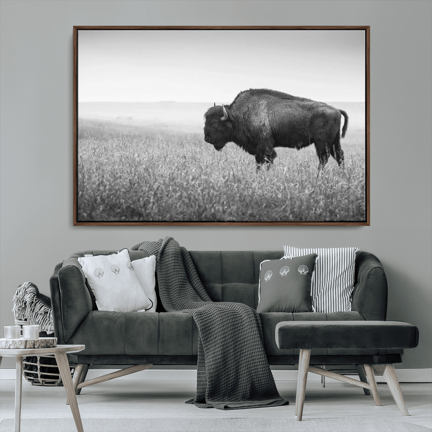 "Black and white image of a bison grazing in a vast field under an overcast sky."