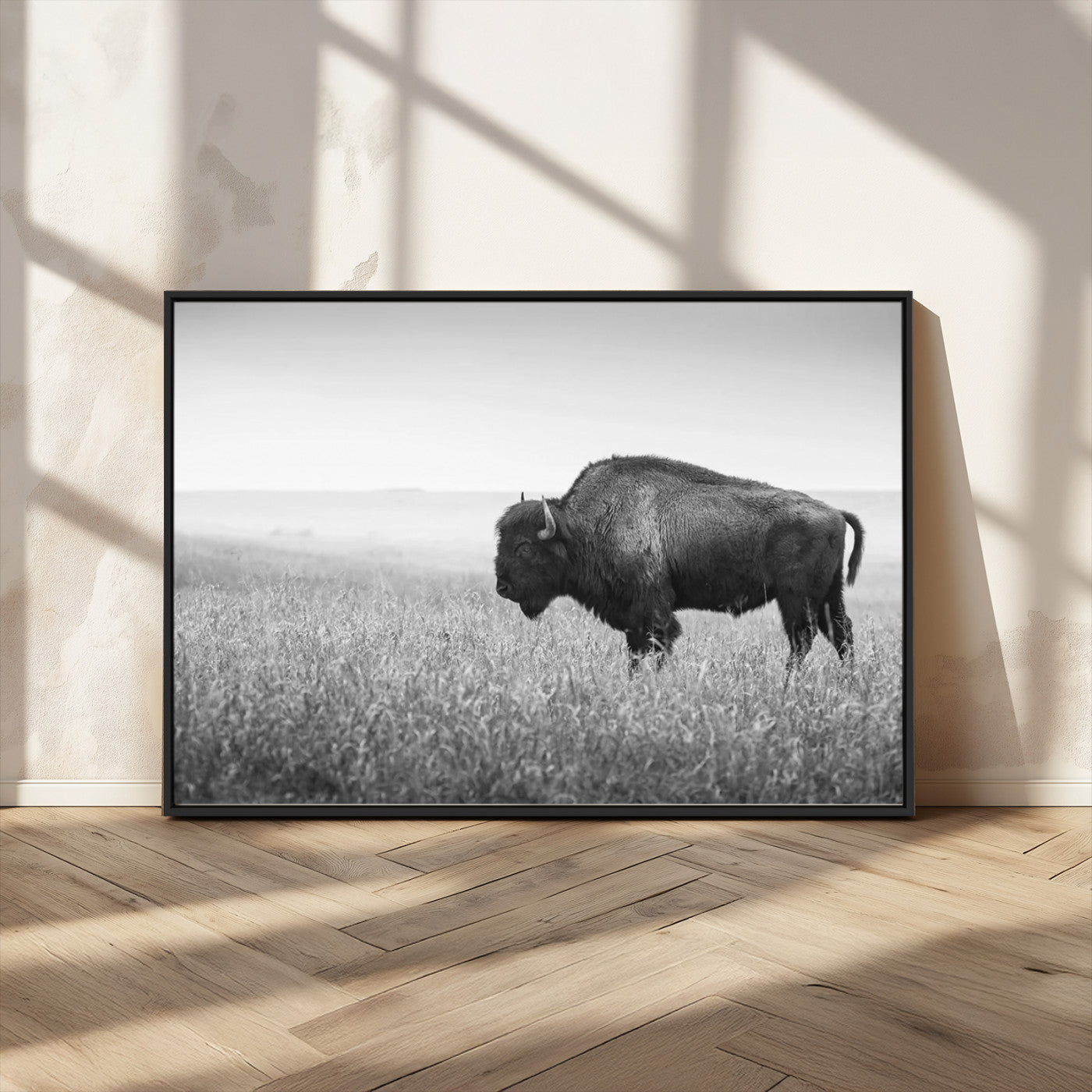 "Black and white image of a bison grazing in a vast field under an overcast sky."