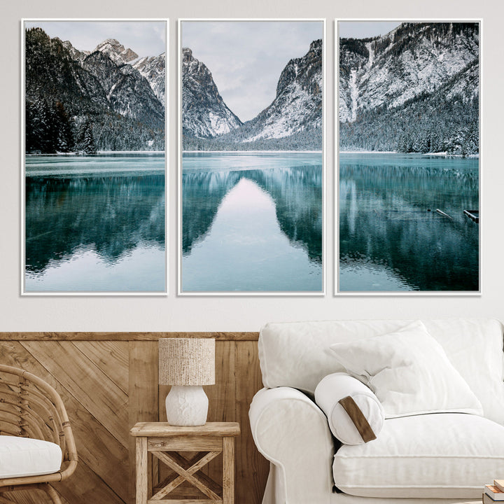Crystal-clear alpine lake reflecting snow-covered mountains, surrounded by evergreen trees, creating a serene and tranquil winter landscape.