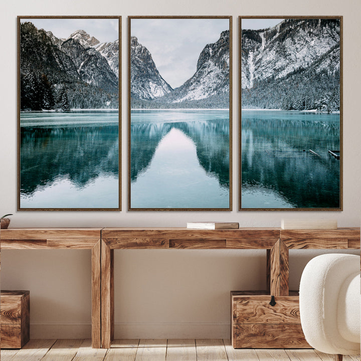 Crystal-clear alpine lake reflecting snow-covered mountains, surrounded by evergreen trees, creating a serene and tranquil winter landscape.
