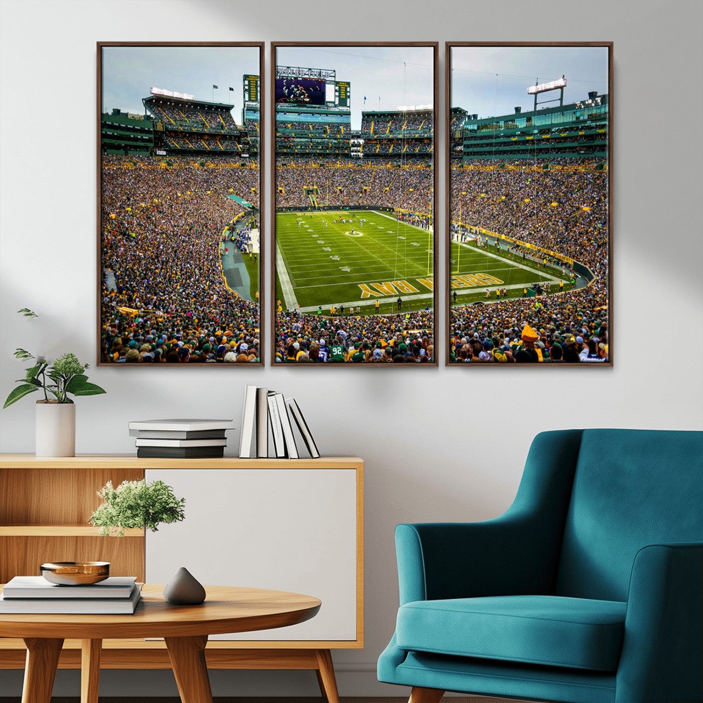 Packed football stadium with thousands of fans watching an American football game on a well-maintained field. The scoreboard displays "Lambeau Field," and players are lined up on the field. The stadium is surrounded by multiple tiers of seating filled wit