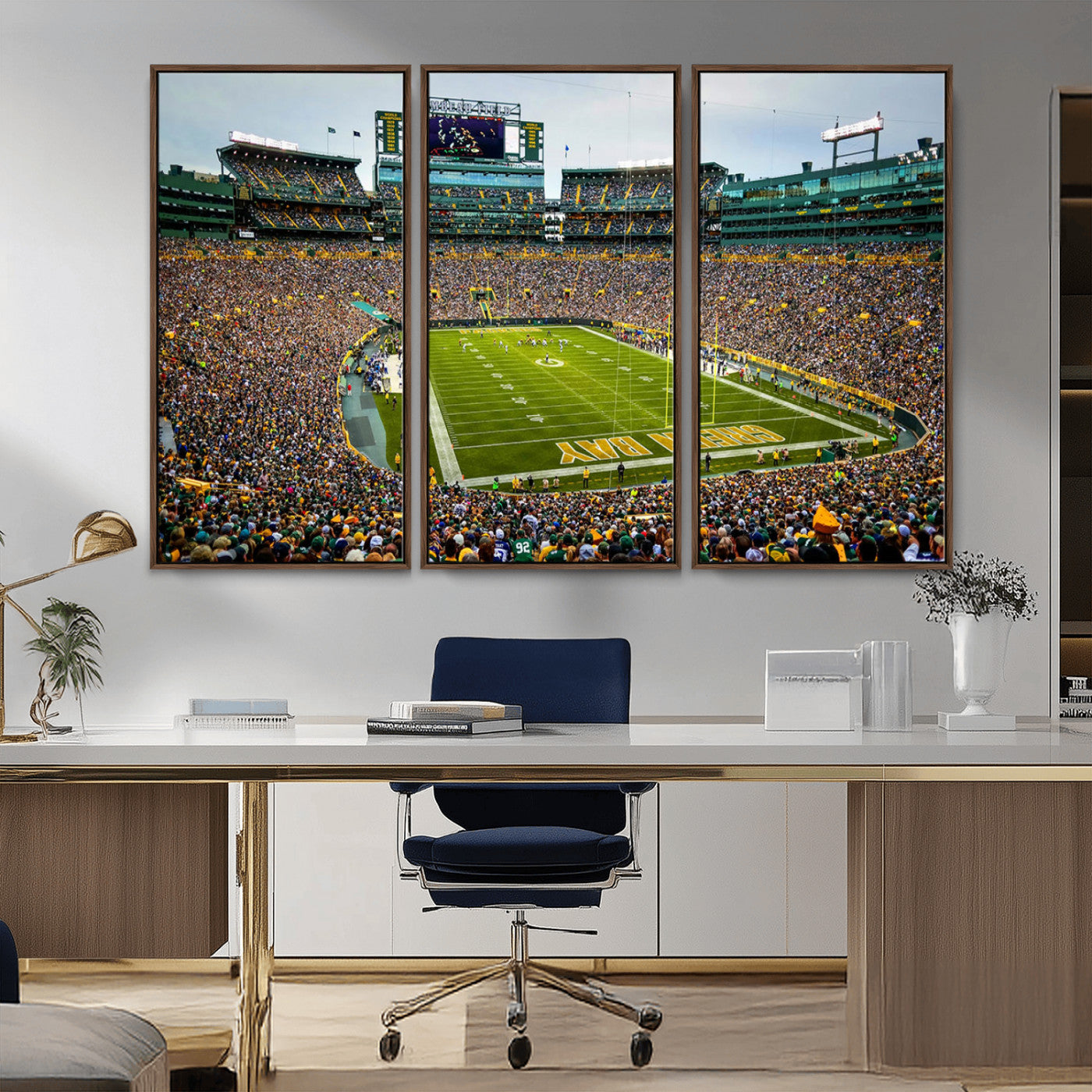 Packed football stadium with thousands of fans watching an American football game on a well-maintained field. The scoreboard displays "Lambeau Field," and players are lined up on the field. The stadium is surrounded by multiple tiers of seating filled wit