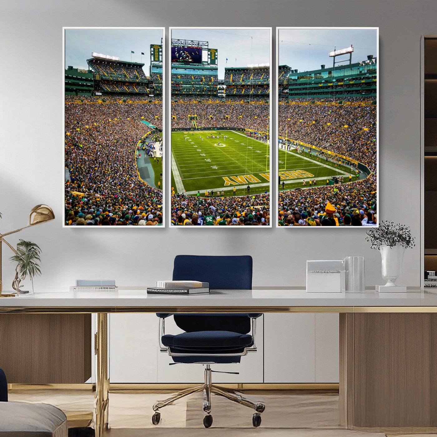 Packed football stadium with thousands of fans watching an American football game on a well-maintained field. The scoreboard displays "Lambeau Field," and players are lined up on the field. The stadium is surrounded by multiple tiers of seating filled wit