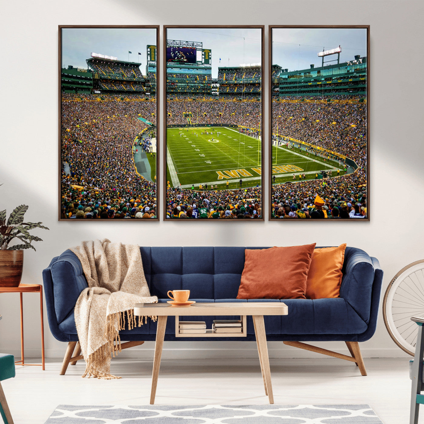 Packed football stadium with thousands of fans watching an American football game on a well-maintained field. The scoreboard displays "Lambeau Field," and players are lined up on the field. The stadium is surrounded by multiple tiers of seating filled wit