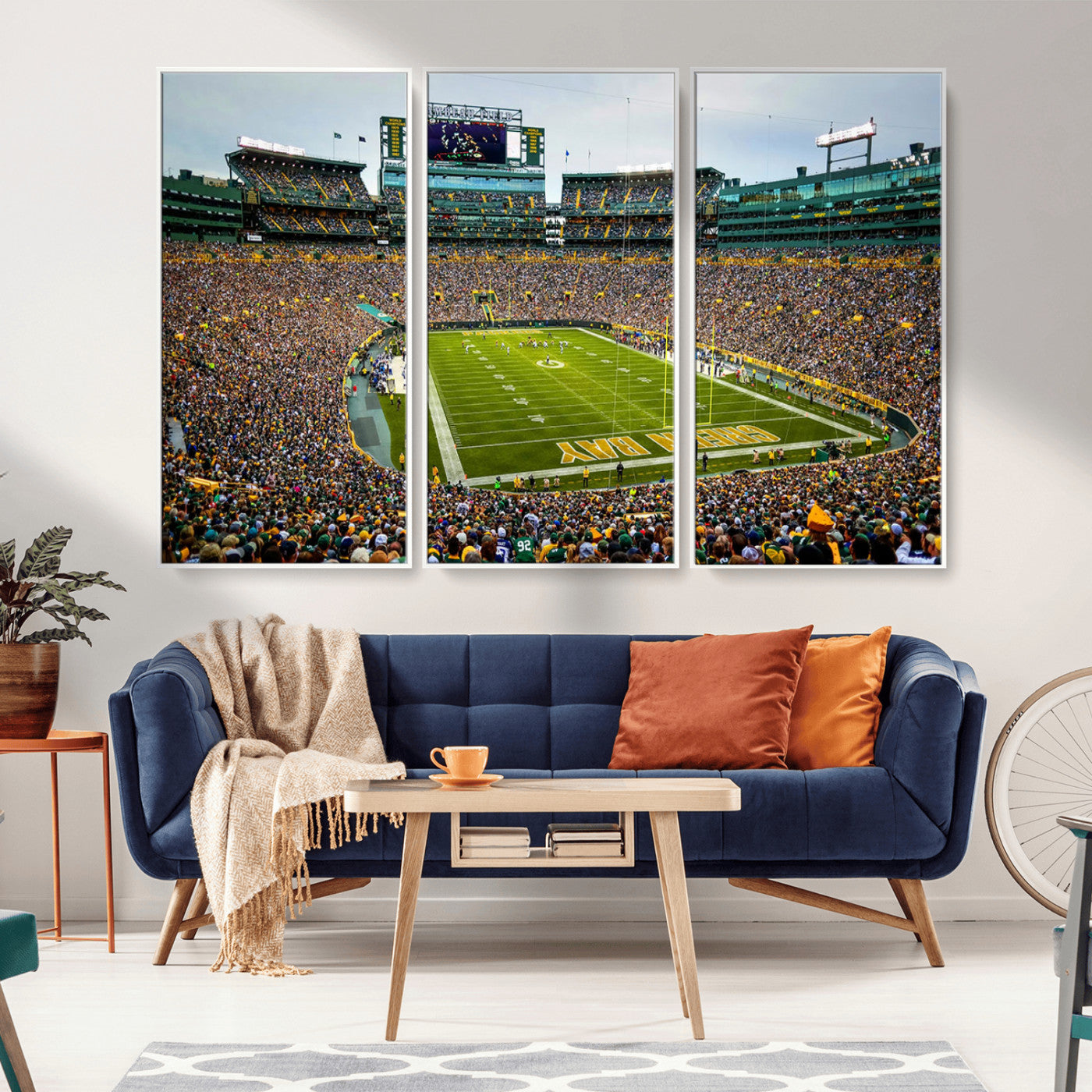 Packed football stadium with thousands of fans watching an American football game on a well-maintained field. The scoreboard displays "Lambeau Field," and players are lined up on the field. The stadium is surrounded by multiple tiers of seating filled wit