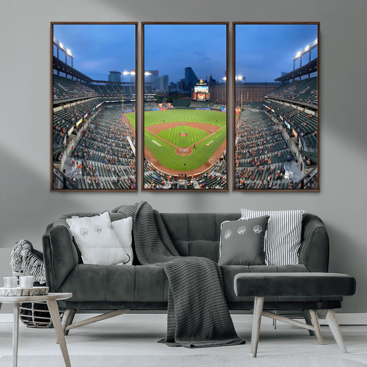 Wide panoramic view of a baseball stadium at dusk with players on the field, stadium lights illuminating the scene, and a sparse crowd of spectators in the stands.