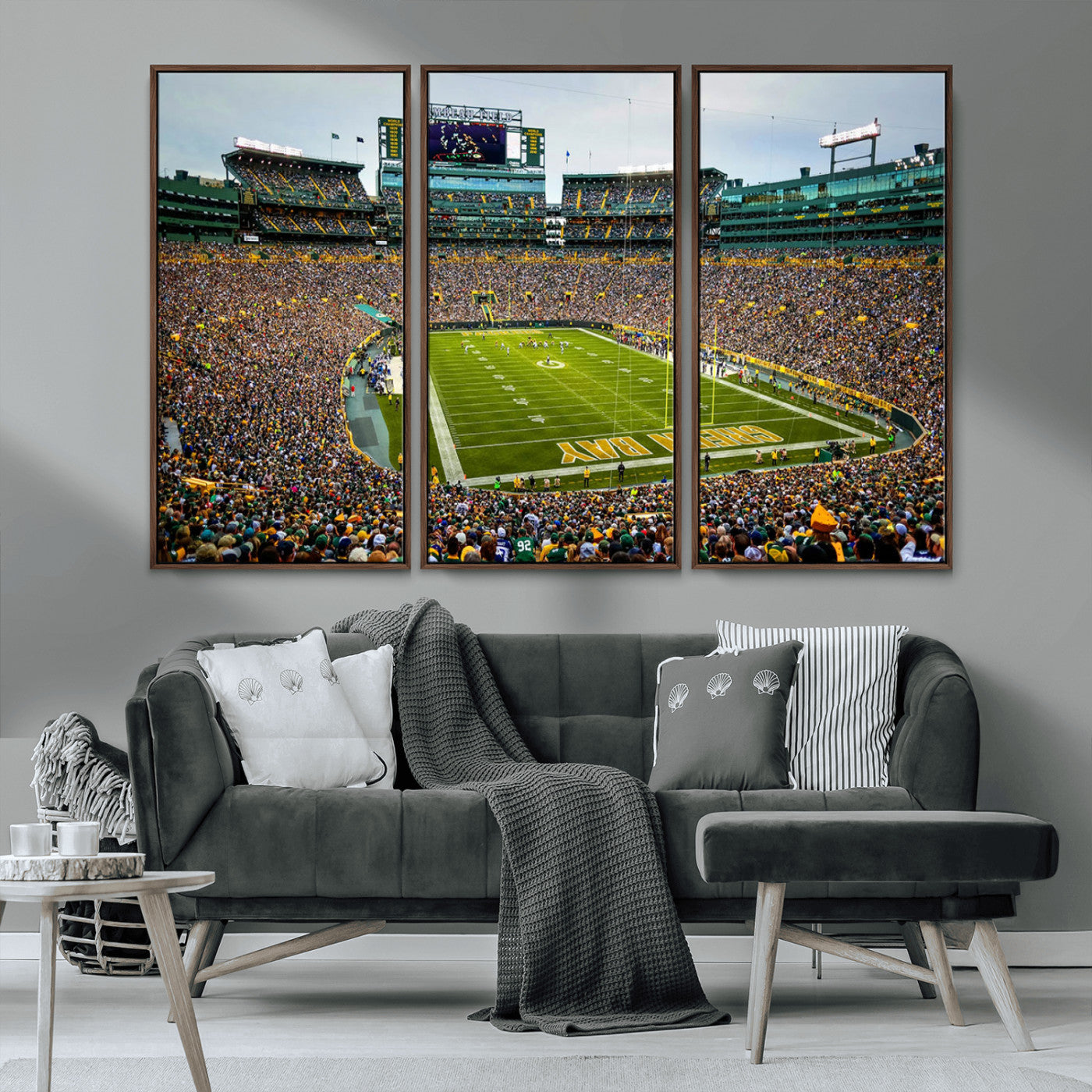 Packed football stadium with thousands of fans watching an American football game on a well-maintained field. The scoreboard displays "Lambeau Field," and players are lined up on the field. The stadium is surrounded by multiple tiers of seating filled wit