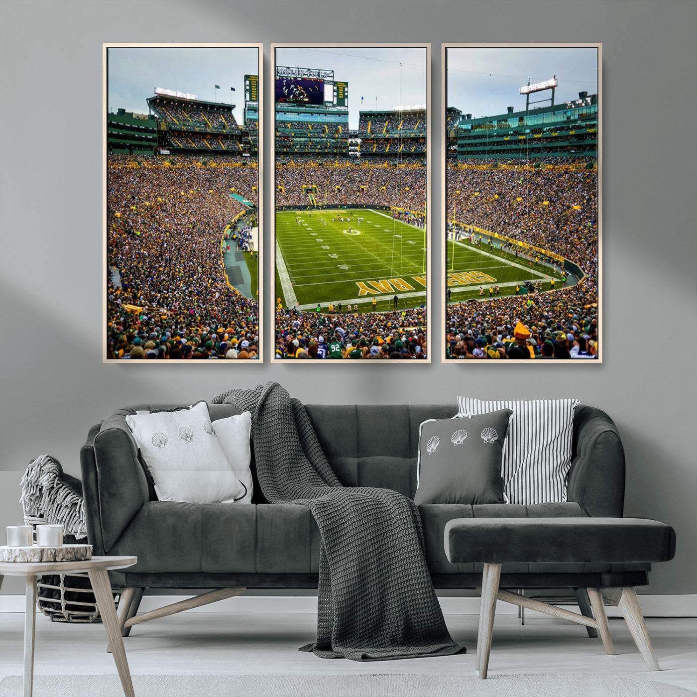 Packed football stadium with thousands of fans watching an American football game on a well-maintained field. The scoreboard displays "Lambeau Field," and players are lined up on the field. The stadium is surrounded by multiple tiers of seating filled wit