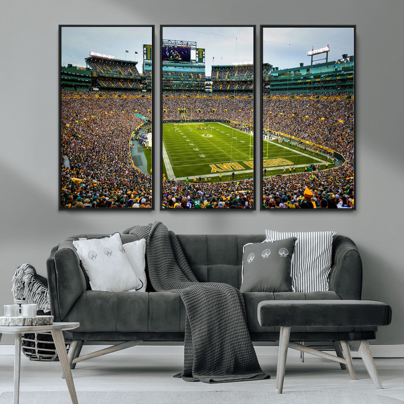 Packed football stadium with thousands of fans watching an American football game on a well-maintained field. The scoreboard displays "Lambeau Field," and players are lined up on the field. The stadium is surrounded by multiple tiers of seating filled wit