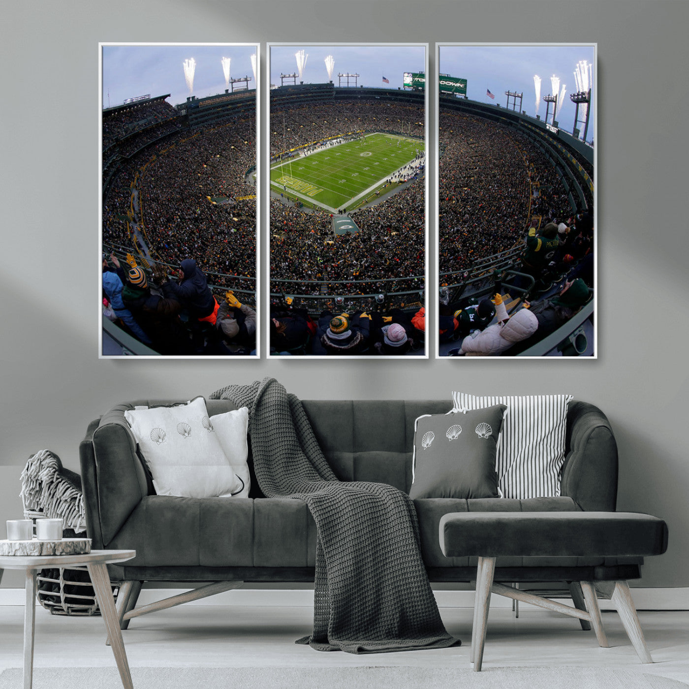 Wide fisheye view of a packed Lambeau Field stadium during an American football game. The crowd fills the stands, and fireworks are going off above the stadium lights. The scoreboard displays "Touchdown," and the field has "Packers" painted in the end zon