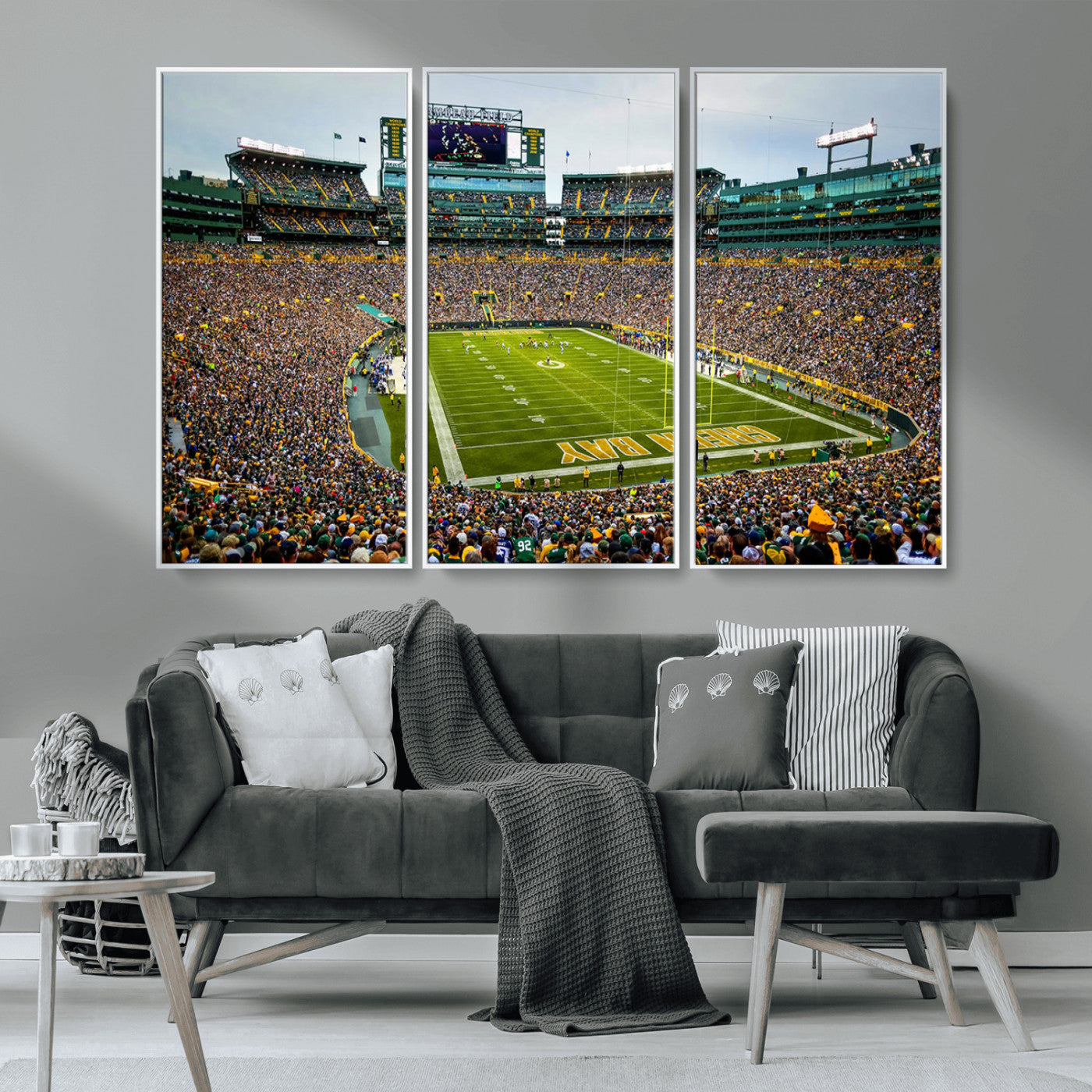 Packed football stadium with thousands of fans watching an American football game on a well-maintained field. The scoreboard displays "Lambeau Field," and players are lined up on the field. The stadium is surrounded by multiple tiers of seating filled wit