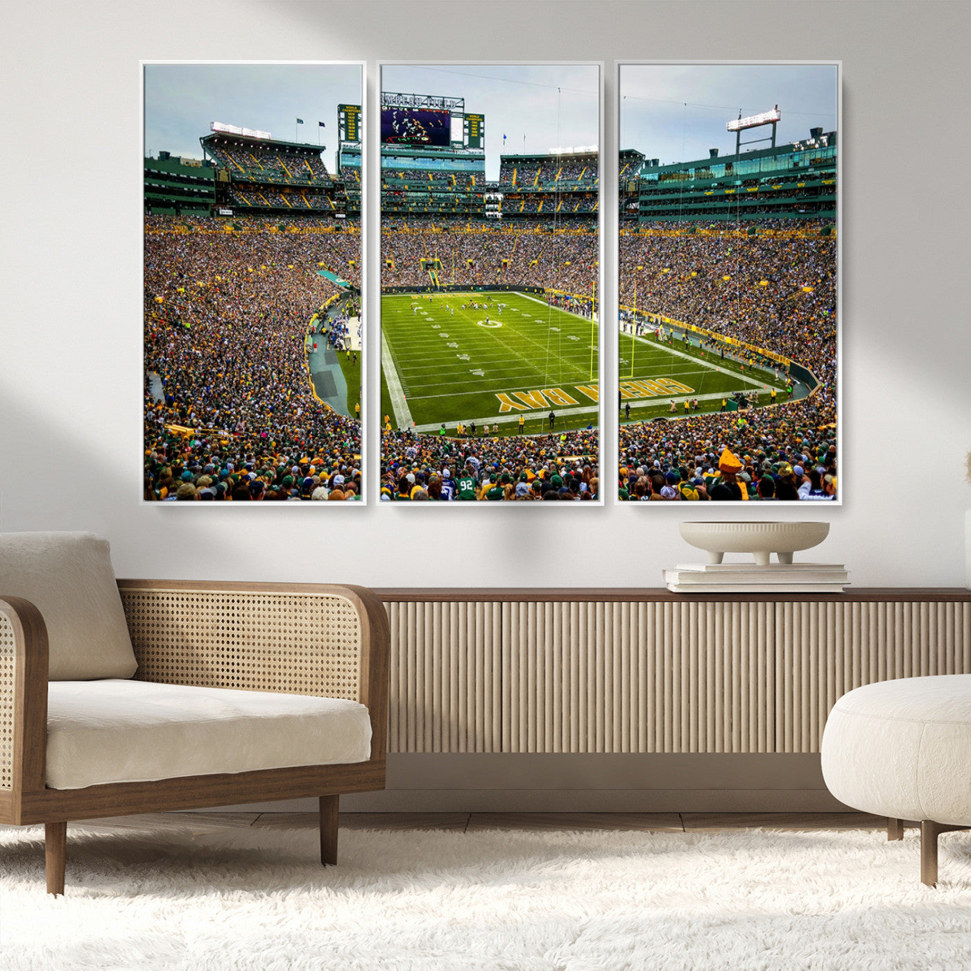 Packed football stadium with thousands of fans watching an American football game on a well-maintained field. The scoreboard displays "Lambeau Field," and players are lined up on the field. The stadium is surrounded by multiple tiers of seating filled wit