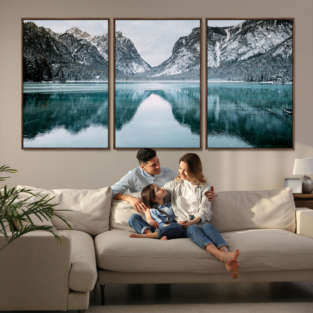 Crystal-clear alpine lake reflecting snow-covered mountains, surrounded by evergreen trees, creating a serene and tranquil winter landscape.