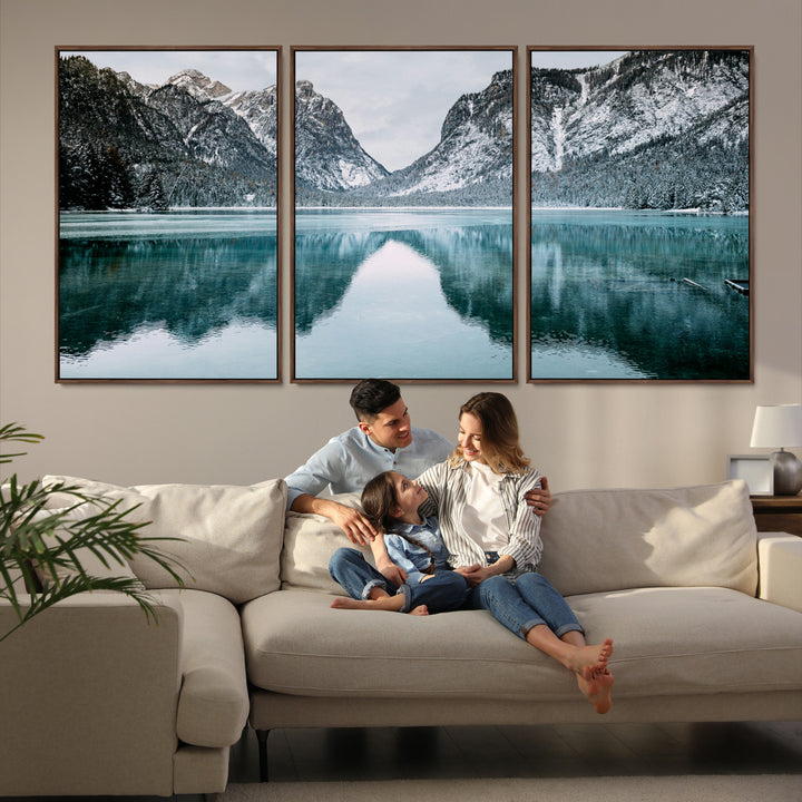 Crystal-clear alpine lake reflecting snow-covered mountains, surrounded by evergreen trees, creating a serene and tranquil winter landscape.
