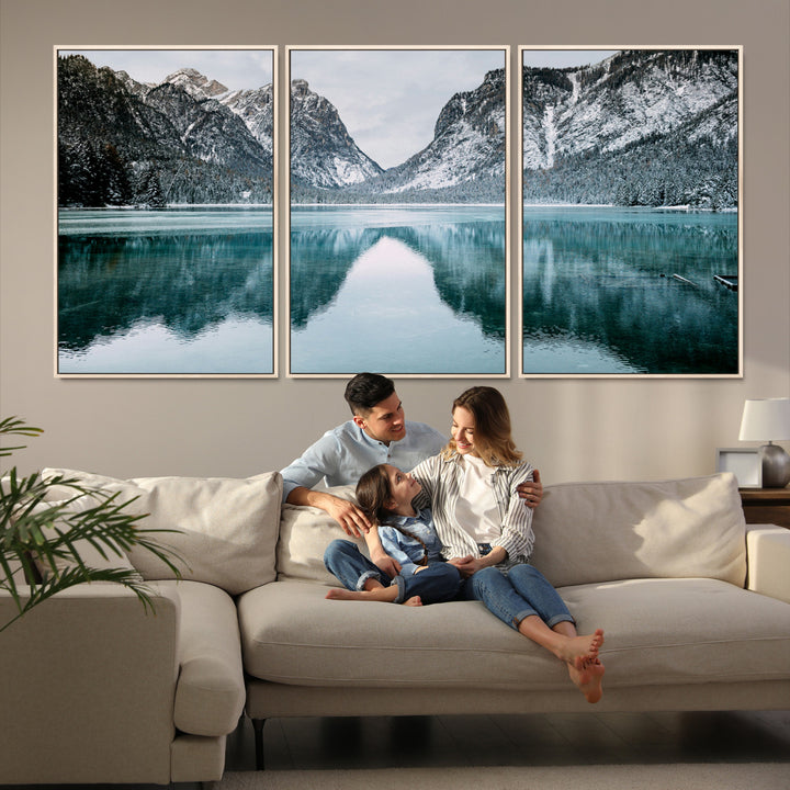 Crystal-clear alpine lake reflecting snow-covered mountains, surrounded by evergreen trees, creating a serene and tranquil winter landscape.